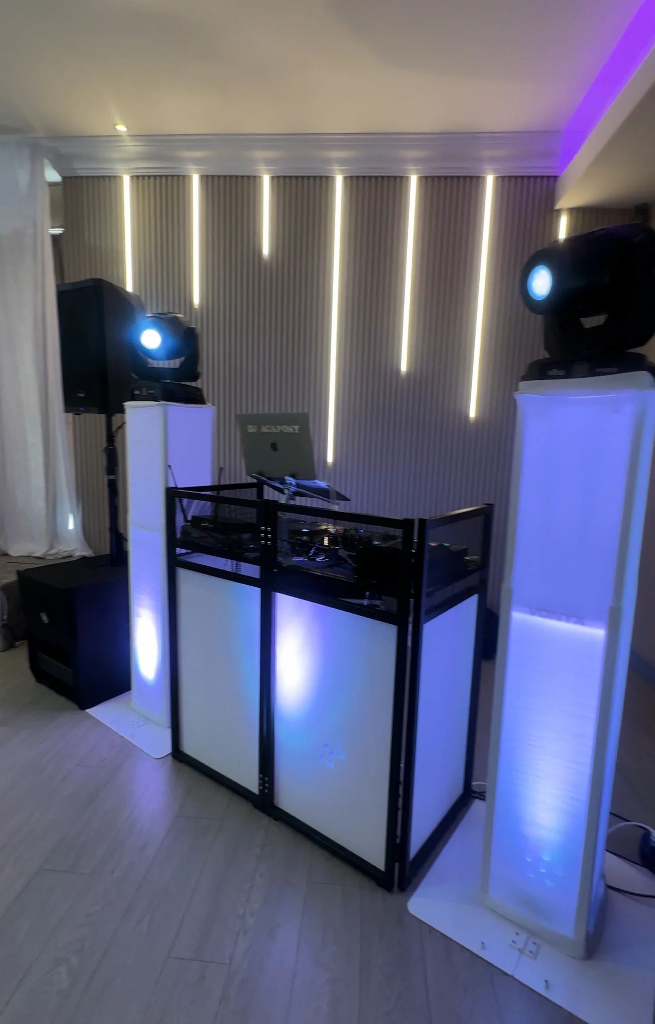 A white DJ booth lit in violet between two moving-head lights