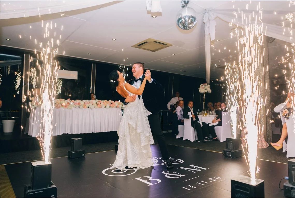 A couple dancing between cold sparks on a dark dancefloor printed with their initials