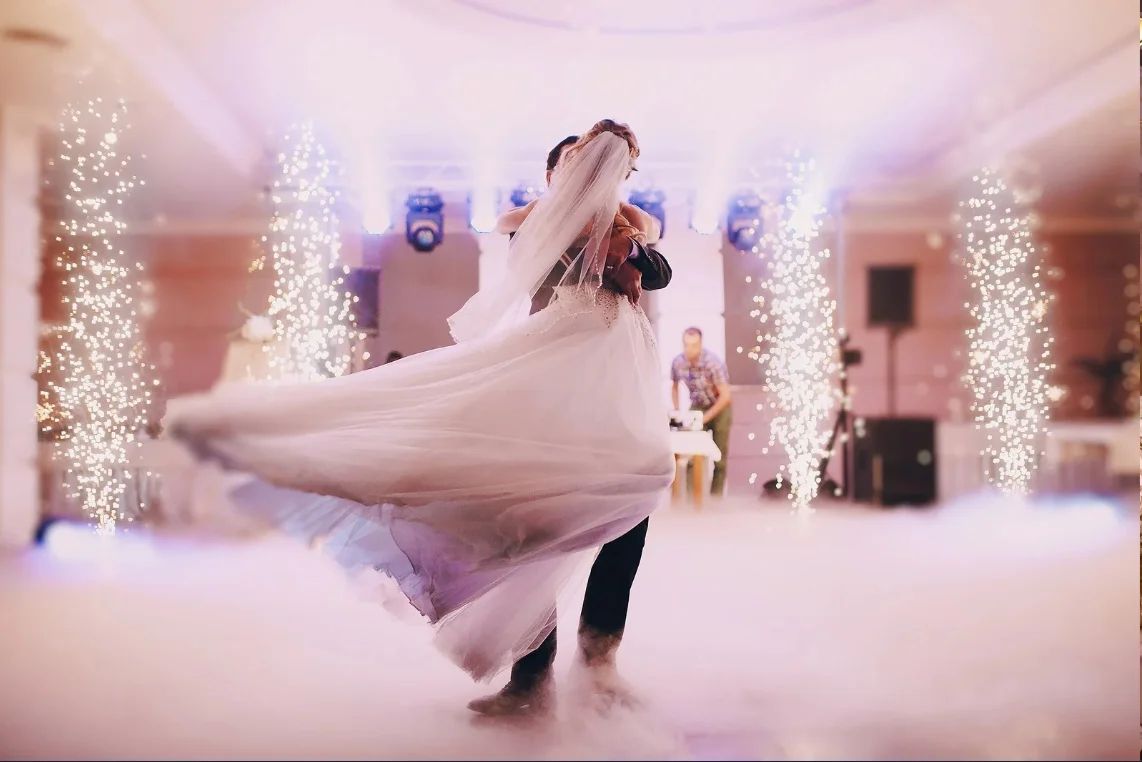 A bride and groom turning on a fog-covered dancefloor between columns of cold sparks