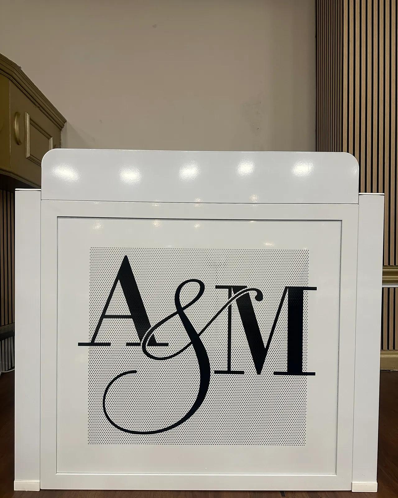 White DJ booth front printed with the couple’s A&M monogram