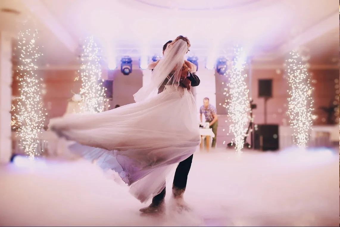 A bride and groom turning on a fog-covered dancefloor between columns of cold sparks