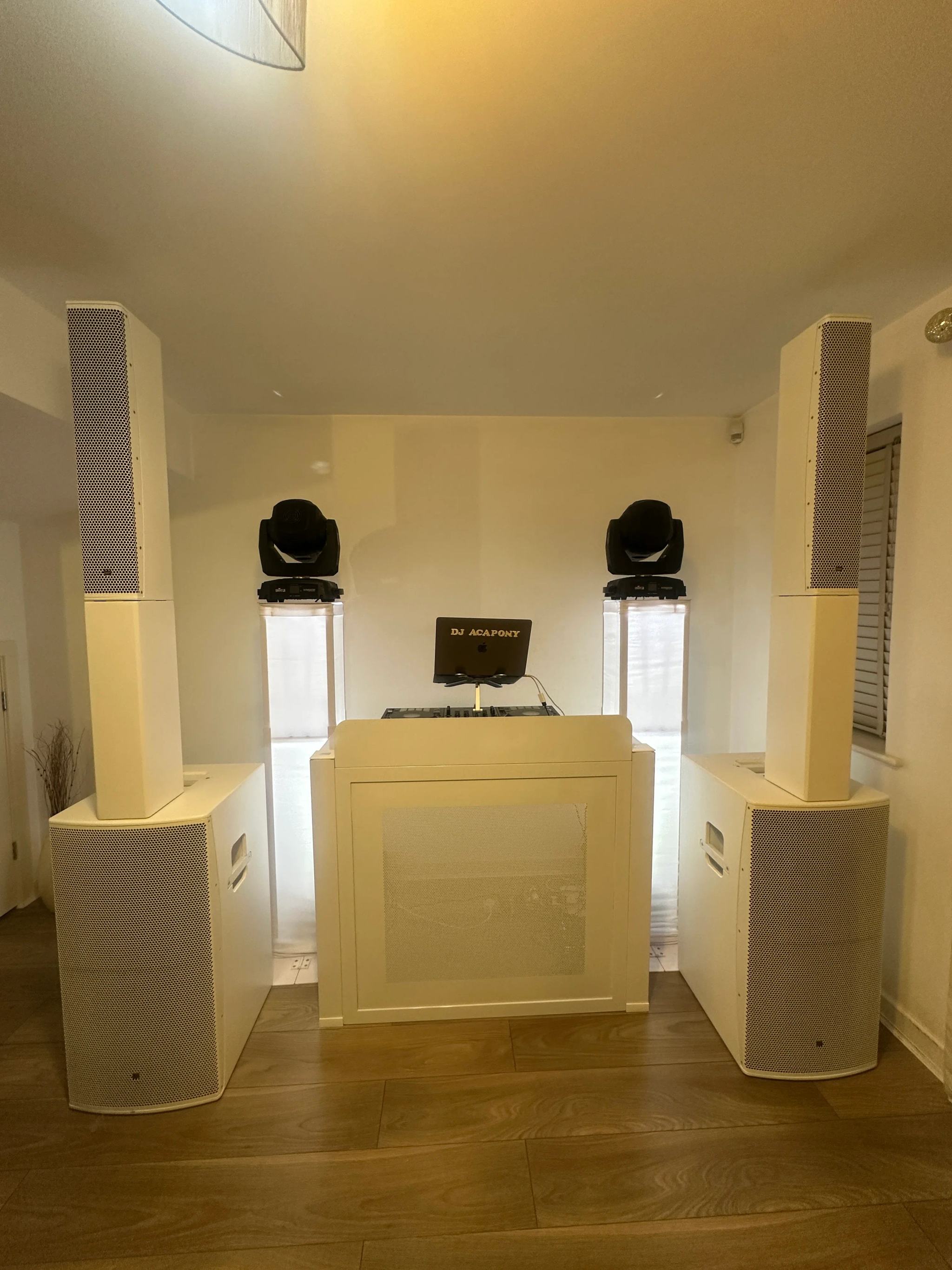 A white DJ booth between tall speakers, with two moving-head lights